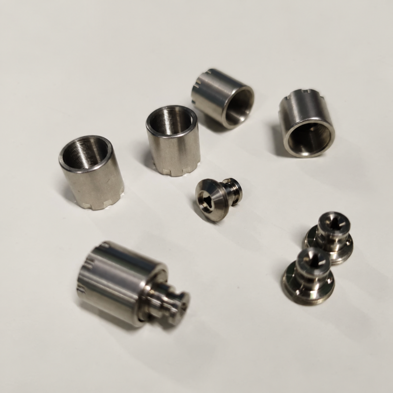 Dispensing nozzle caps and adjustment nuts Metal threaded sleeves and small stepped nozzle components on a pale surface.