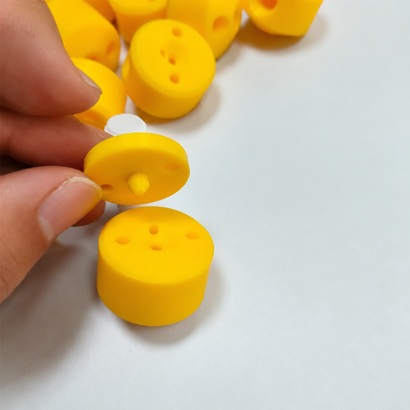Dispensing valve diaphragm and body Yellow valve components, with a hand lifting a round diaphragm above a cylindrical body.
