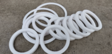 Assorted white PTFE ball valve seat rings overlapping on gray concrete, with two larger rings in the foreground.
