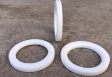 Three white PTFE ball valve seat rings on gray concrete, with two lying flat and one standing upright.