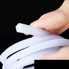 Close-up of hands holding a coiled white solid rectangular silicone strip and its cut end.