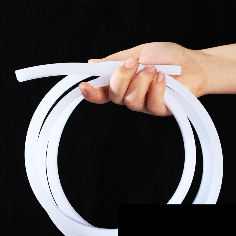 Hand holding a looped white solid square silicone strip against a black background.