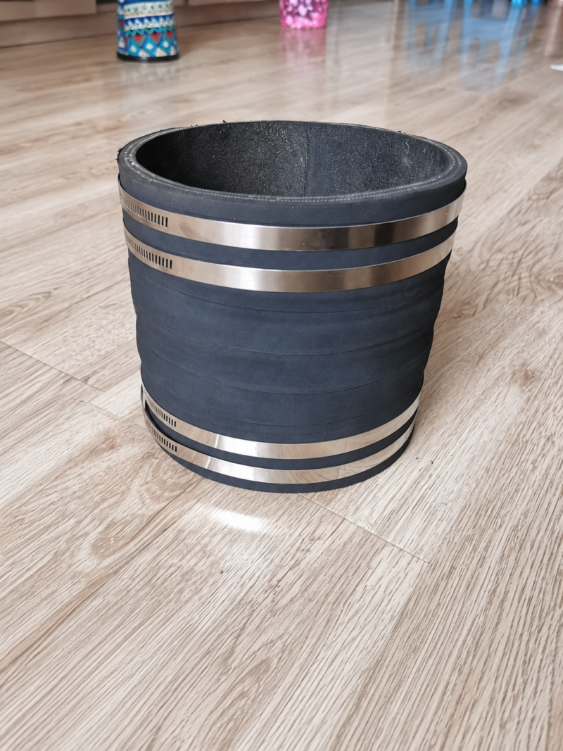Large black cylindrical pipe connector with four metal hose clamps.