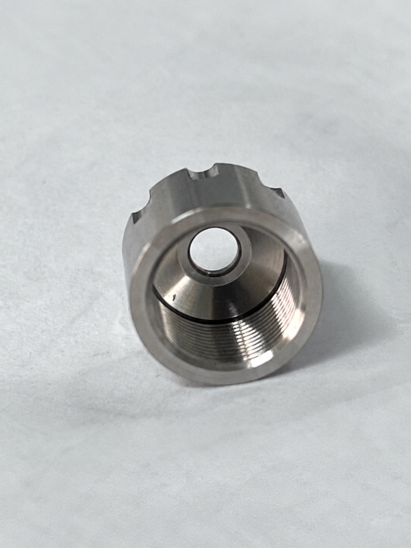 Close-up of a metal nozzle cap showing internal threads, a conical inner face and a central opening.