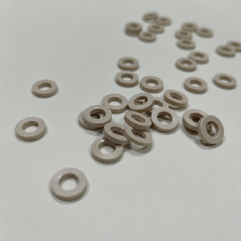 Beige annular gaskets with circular center openings scattered and stacked on a pale surface.