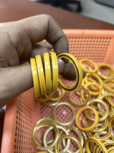 Hand holding yellow sealing rings above an orange basket, showing the ring edges and exposed metal spring.