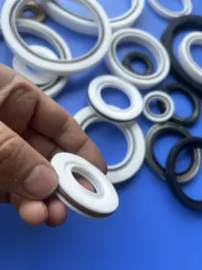A hand holding a white rotary seal, with assorted sealing rings on a blue surface behind it.
