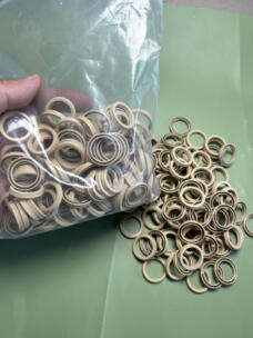 Beige rotary shaft seals with visible metal springs in clear bulk packaging beside loose seals