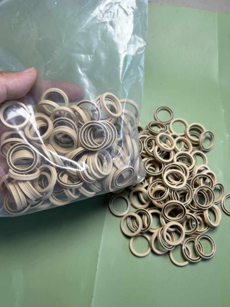 Beige rotary shaft seals with visible metal springs in clear bulk packaging beside loose seals