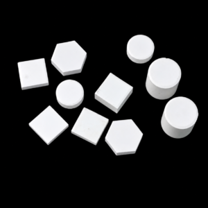 White IKSONIC ceramic square and hexagonal tiles, round discs and cylindrical pieces arranged on a black background.