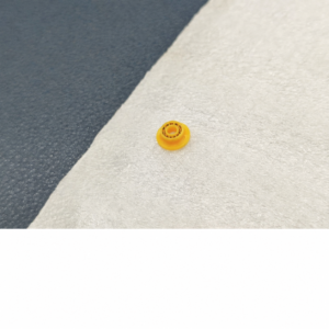 IKSONIC yellow analyzer plunger seal with a raised center and small ring details on a white cloth.