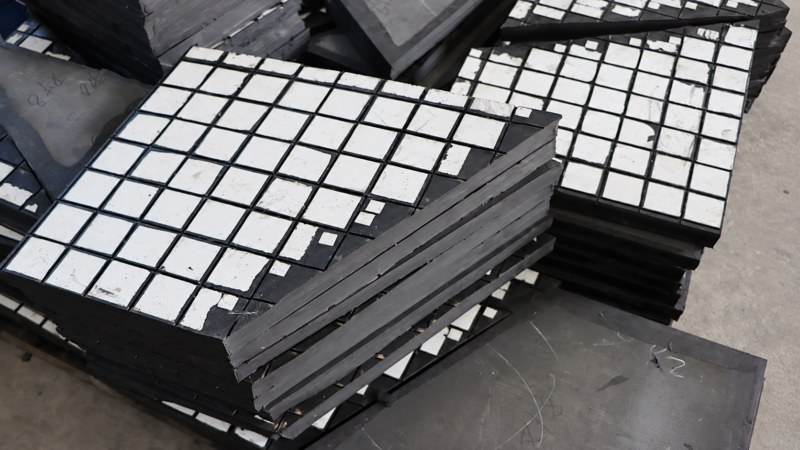Overlapping IKSONIC ceramic rubber liner panels showing white tiles and thick dark backing edges.