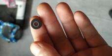 A small black flanged seal with a circular metal spring resting on a fingertip; supplied by IKSONIC in China.