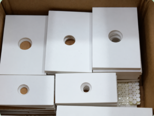 Stacked white IKSONIC ceramic liner plates with five visible mounting holes in a box.