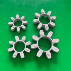 Four grey eight-lobed jaw-coupling spider inserts with circular center openings and molded markings on a green surface.