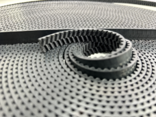 Curved open end of a black herringbone elevator door belt on a coil, IKSONIC wholesale supply.