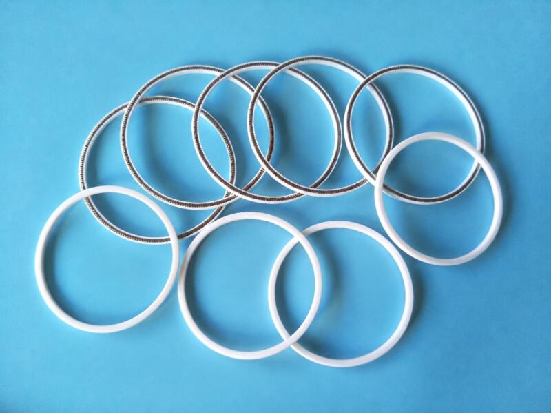 White IKSONIC seal rings and spring-equipped PTFE rings arranged on a blue background.