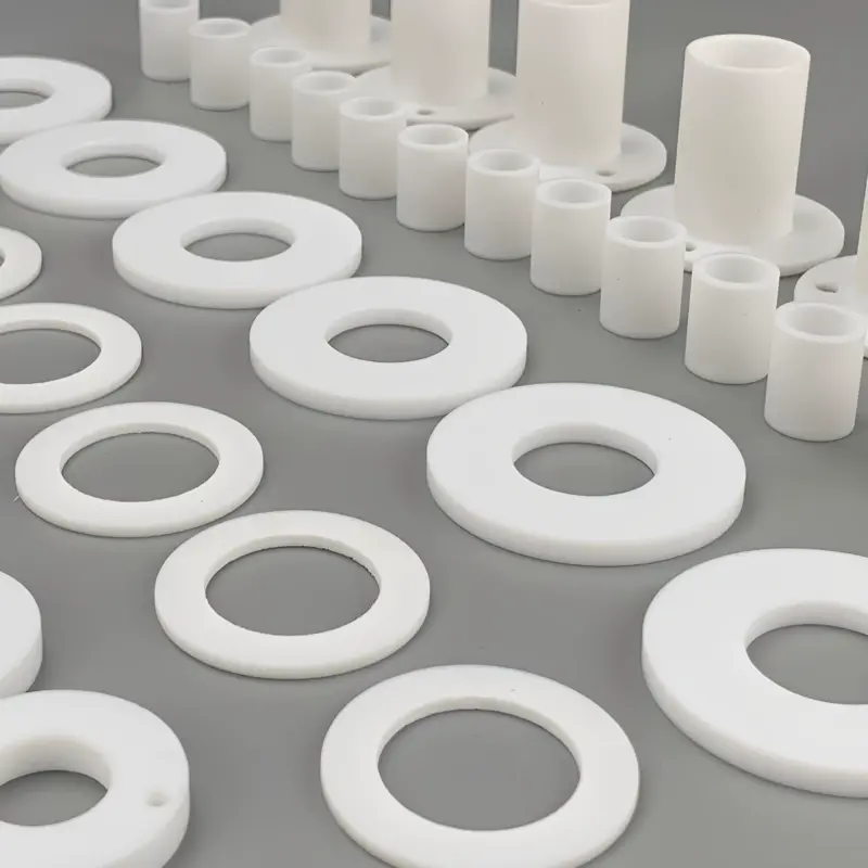 White PTFE flat sealing rings, cylindrical sleeves and flanged sleeves arranged on a gray surface; supplied by IKSONIC in China.