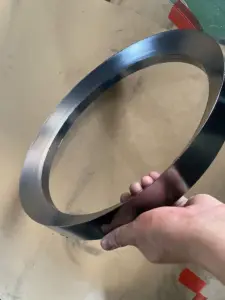 Large smooth-faced IKSONIC graphite packing ring held at an angle above a cardboard surface.