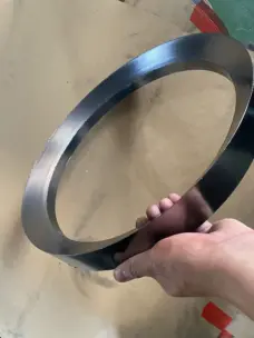 Large smooth-faced graphite packing ring held at an angle above a cardboard surface.