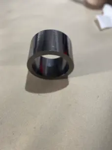 Single tall smooth-faced graphite packing ring resting on a cardboard surface.