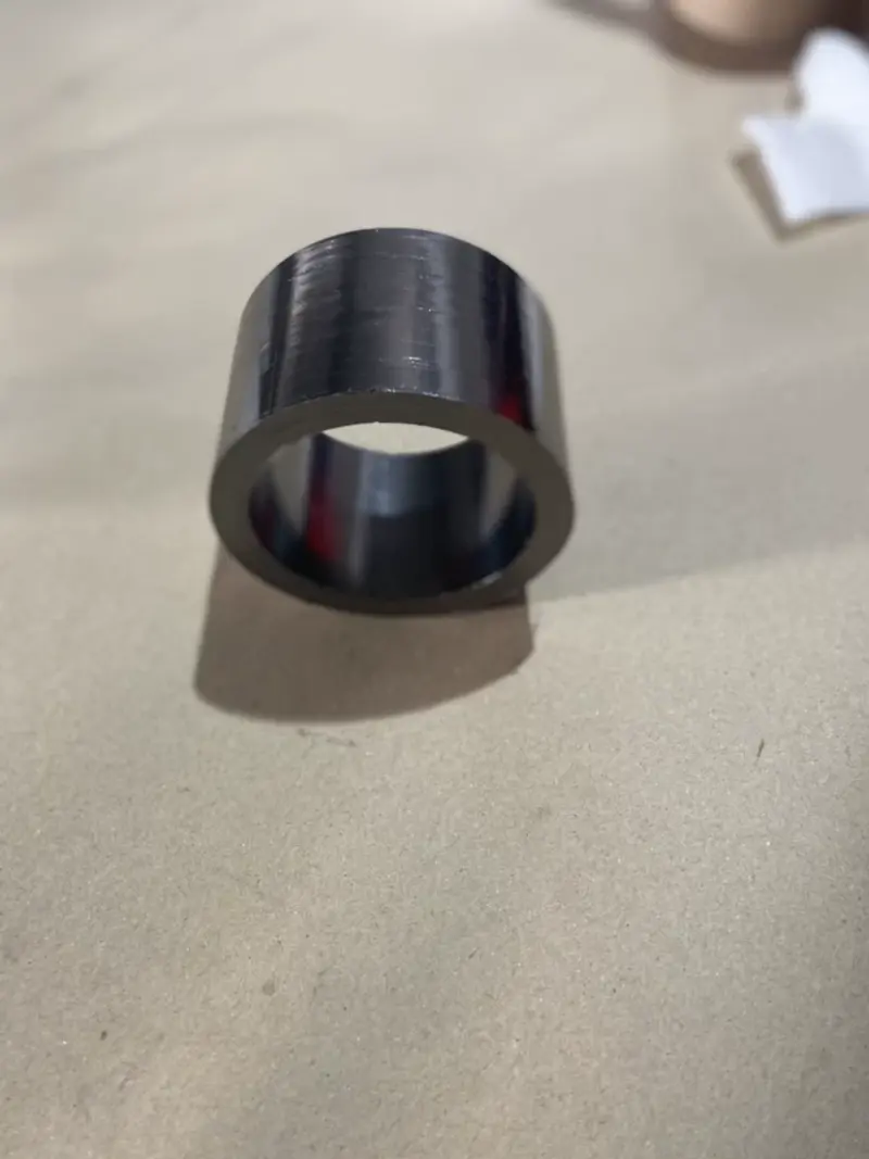 Single tall smooth-faced graphite packing ring resting on a cardboard surface.