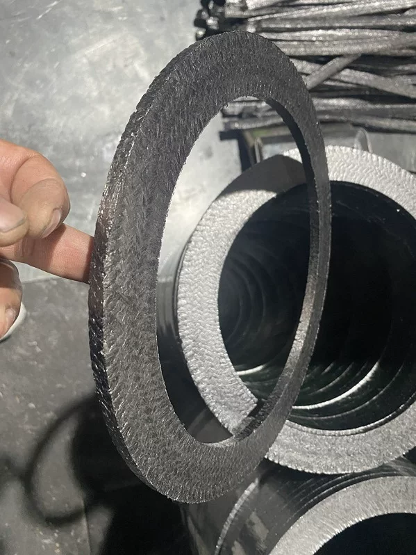 Graphite packing ring held upright, showing its face and thin edge with other rings in the background.