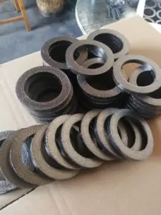 Assorted graphite packing rings arranged in stacks and overlapping rows on a cardboard surface.
