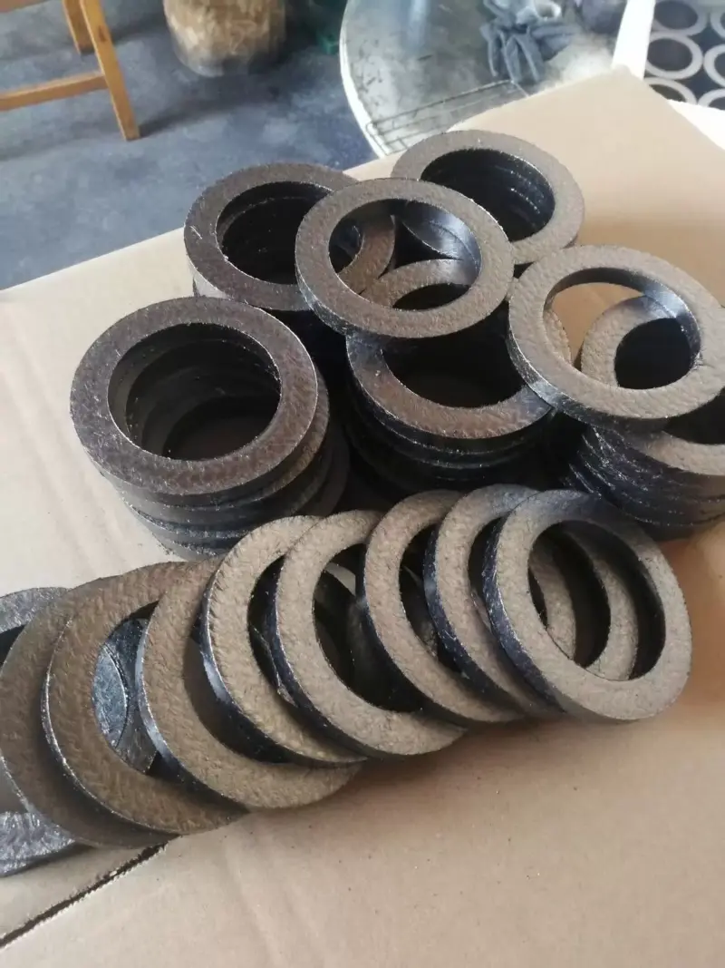 iksonic-supplier-graphite-braided-packing-rings-assortment Assorted graphite packing rings arranged in stacks and overlapping rows on a cardboard surface.