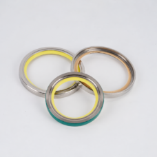 Three overlapping vacuum pump shaft seal rings supplied by IKSONIC, with a yellow inner edge at rear left, a tan inner edge at rear right, and a green outer edge on the front ring.