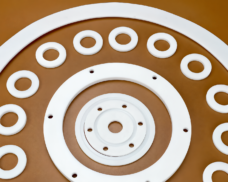 White PTFE flange gaskets and flat sealing rings arranged on a brown background; supplied by IKSONIC in China.