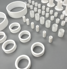 White PTFE sleeves, flanged bushings and stepped rings on a gray surface, an IKSONIC China supplier reference assortment.