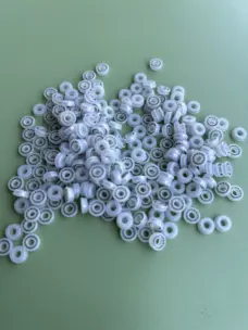 Small translucent white jetting valve seals with metal springs on a green surface.