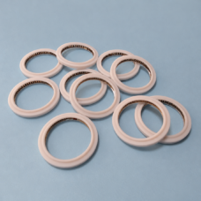 Pale annular sealing rings with visible internal metal springs on a blue-gray surface.