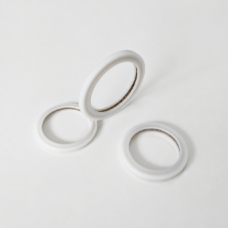 Three white annular sealing rings with fine internal metal springs, including one ring tilted upright.