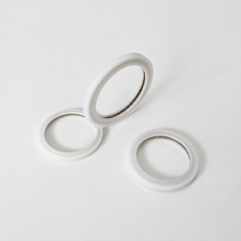 Three white annular sealing rings with fine internal metal springs, including one ring tilted upright.