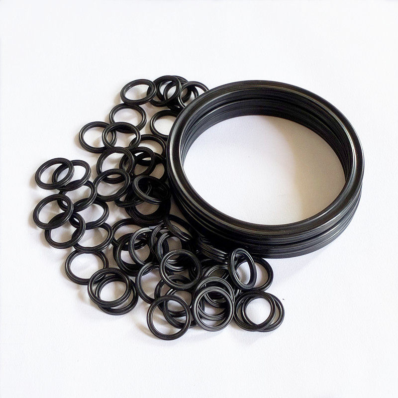 Black sealing rings in assorted sizes next to a stack of larger rings on a white surface.
