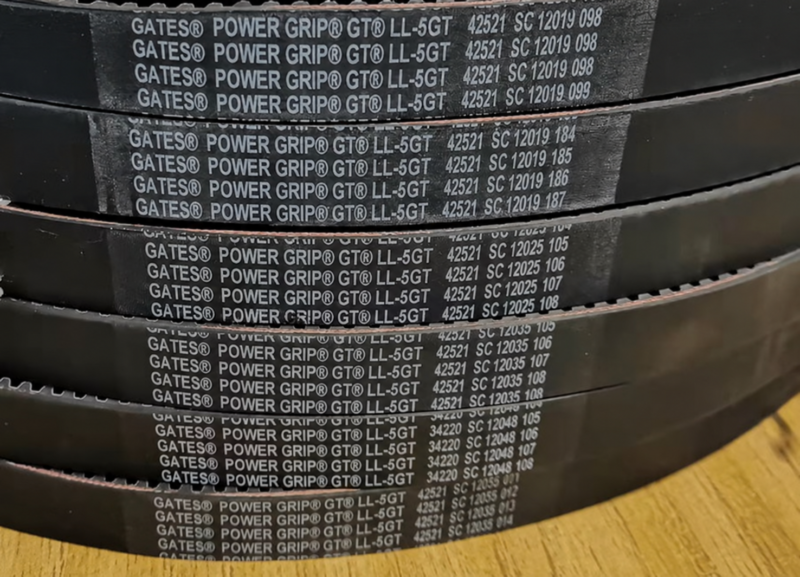Close view of stacked open-ended timing belts showing their printed markings and toothed edges.