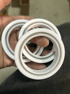 A hand holding three white annular shaft seals with visible circumferential springs.