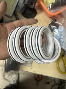 Hand holding several white shaft seals showing their outer dark rings and metal spring channels.